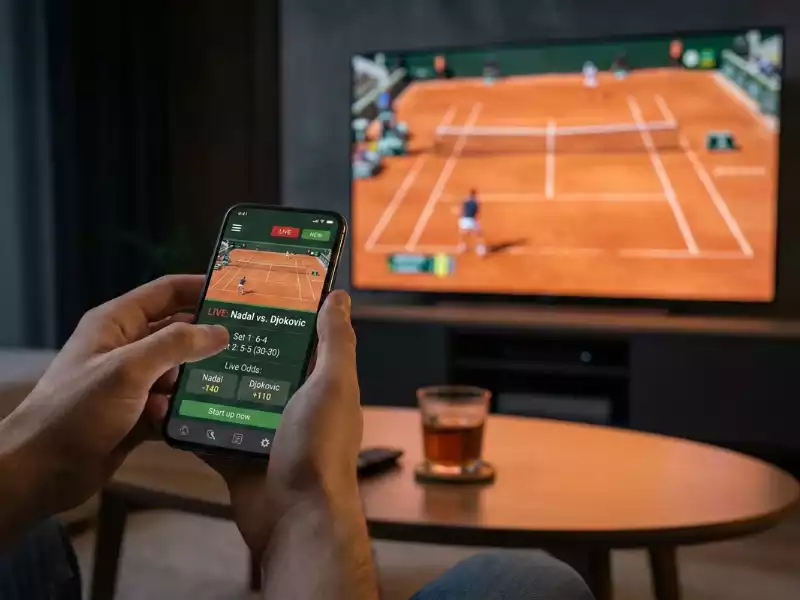 Mãos a segurar smartphone com pontuação de ténis ao vivo e televisão com partida em fundo